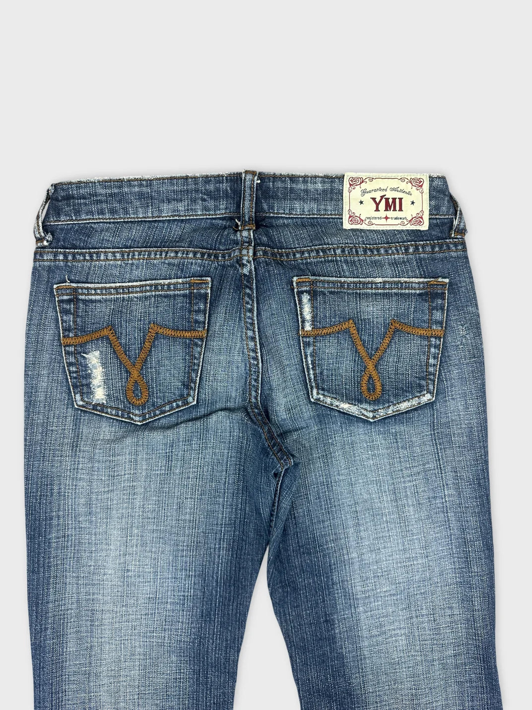 Detail view of blue denim jeans featuring embroidered back pockets.