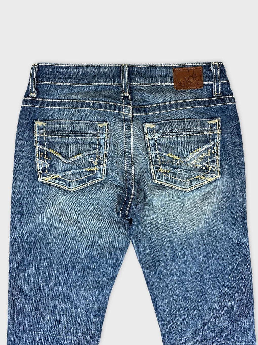 Detail view of blue denim jeans showcasing decorative stitching on back pockets.