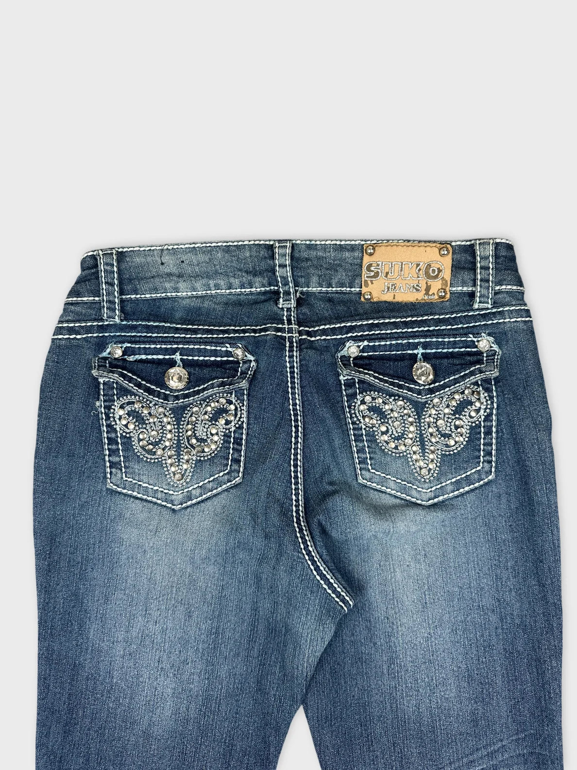 Detail view of dark blue denim jeans featuring decorative back pockets.