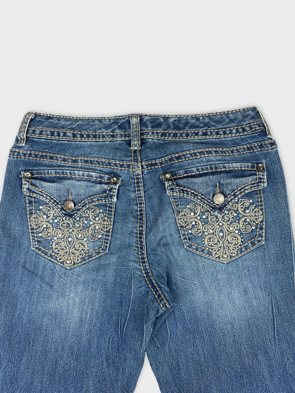 Detail view of blue denim jeans with decorative embroidered back pockets.