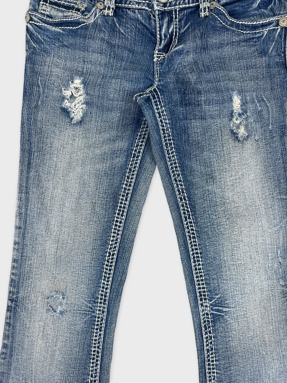 Detail view of blue denim jeans featuring distressed patches and faded edges.