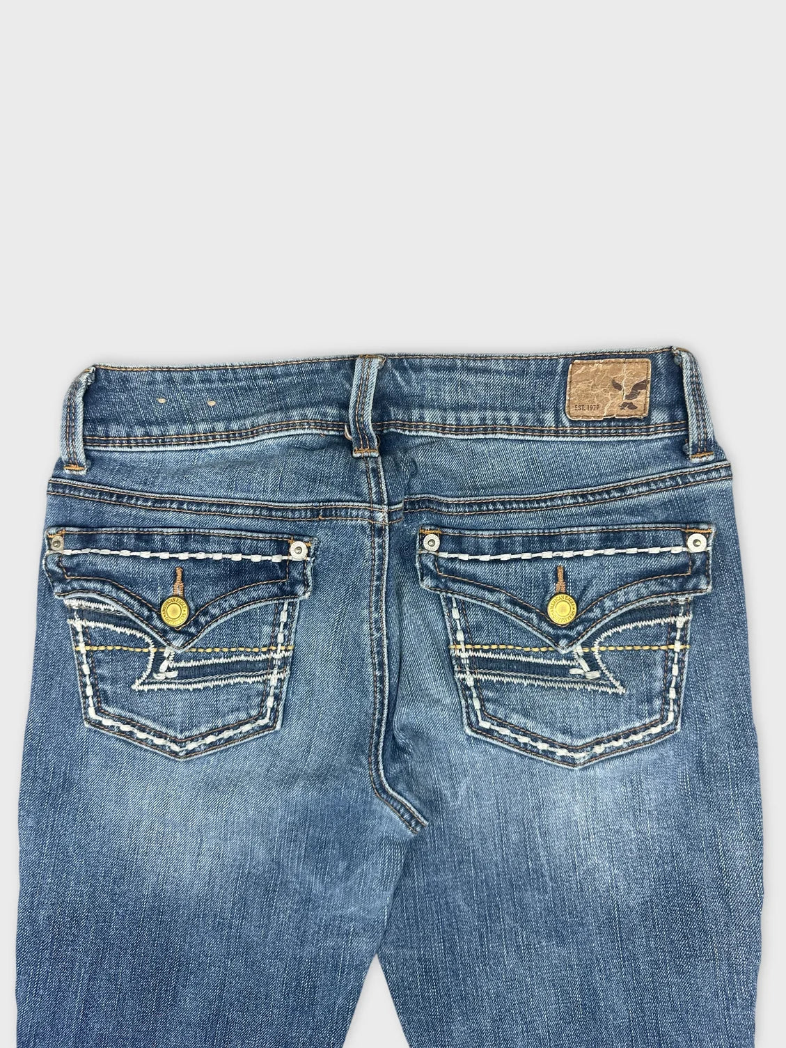 Detail view of blue denim jeans featuring embroidered back pockets