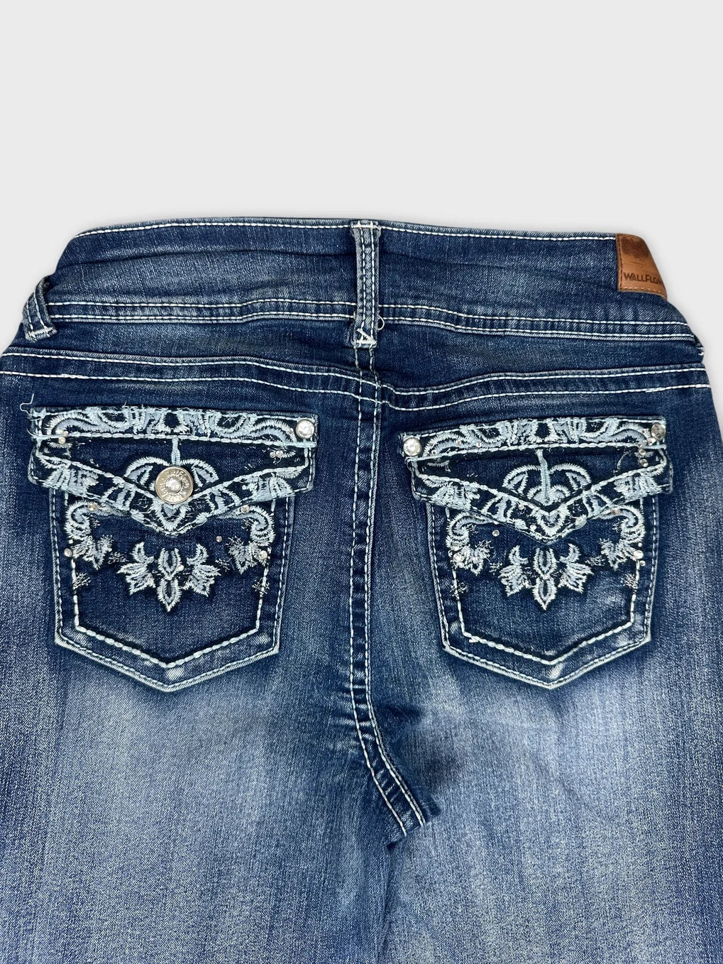 Detail view of dark blue denim jeans featuring embroidered back pockets.