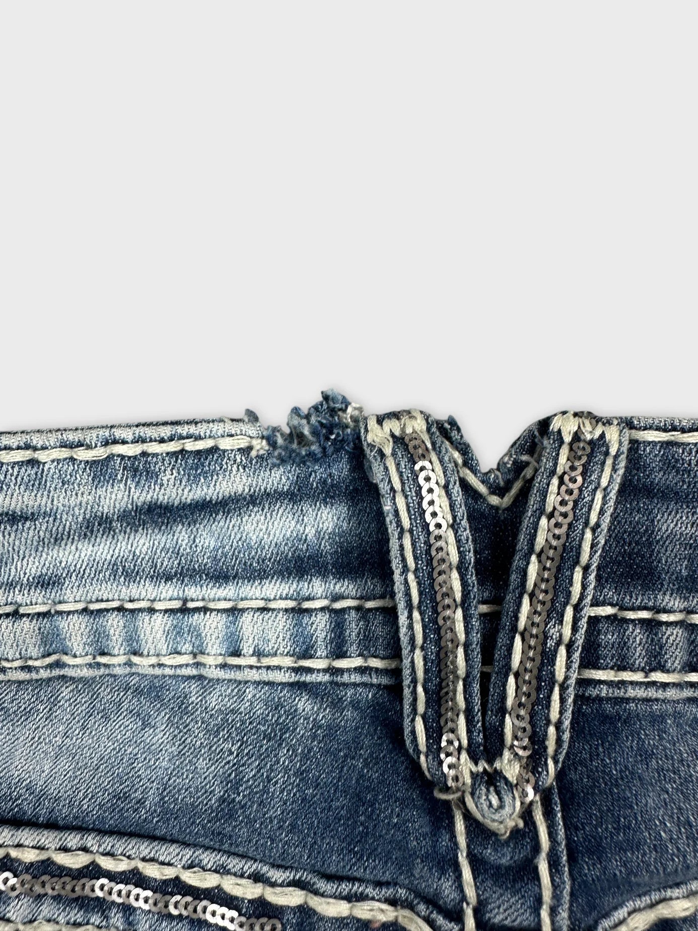 Detail view of blue denim jeans featuring shiny sequined trim on waistband.