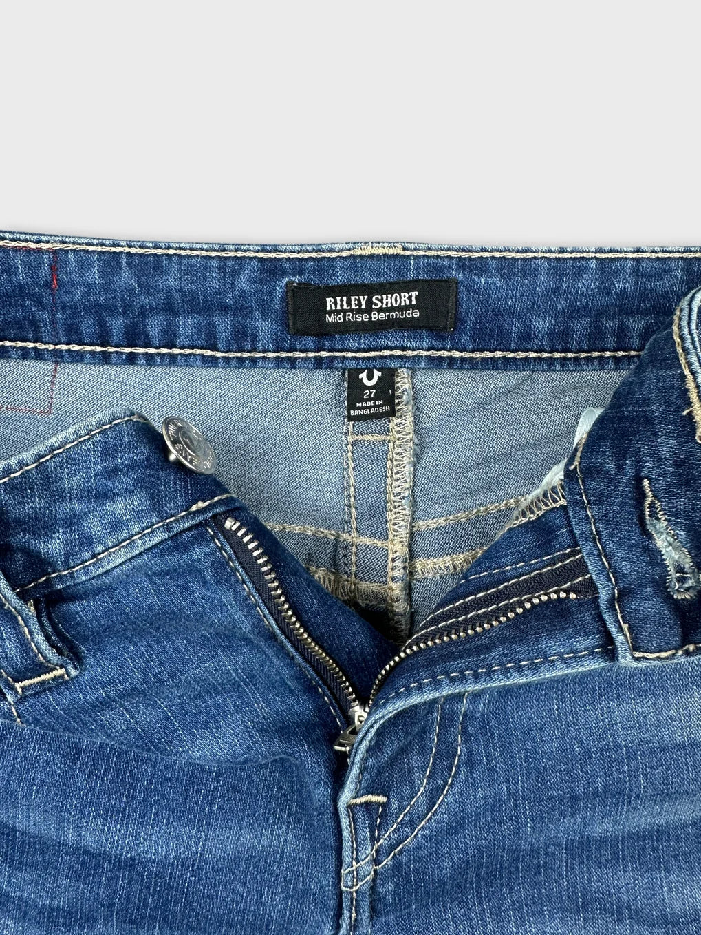 Detail view of blue denim midi shorts featuring a zip closure.