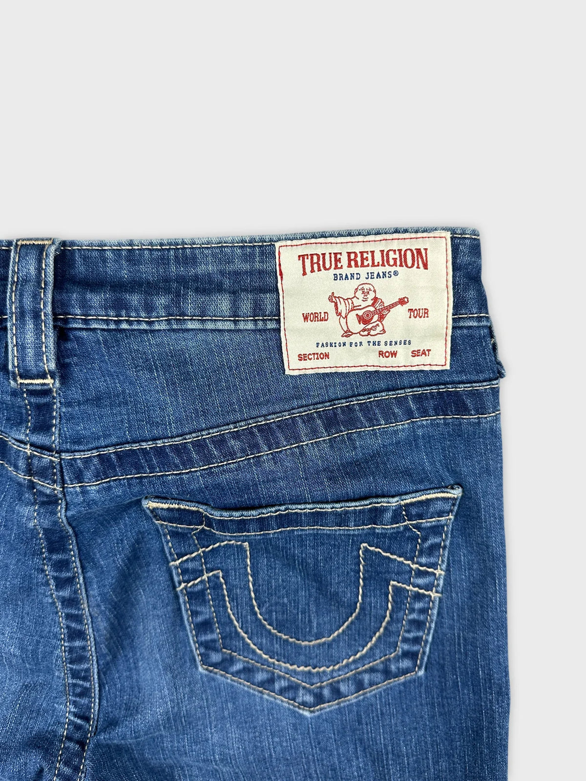 Detail view of women denim midi shorts in blue with stitching and logo patch.