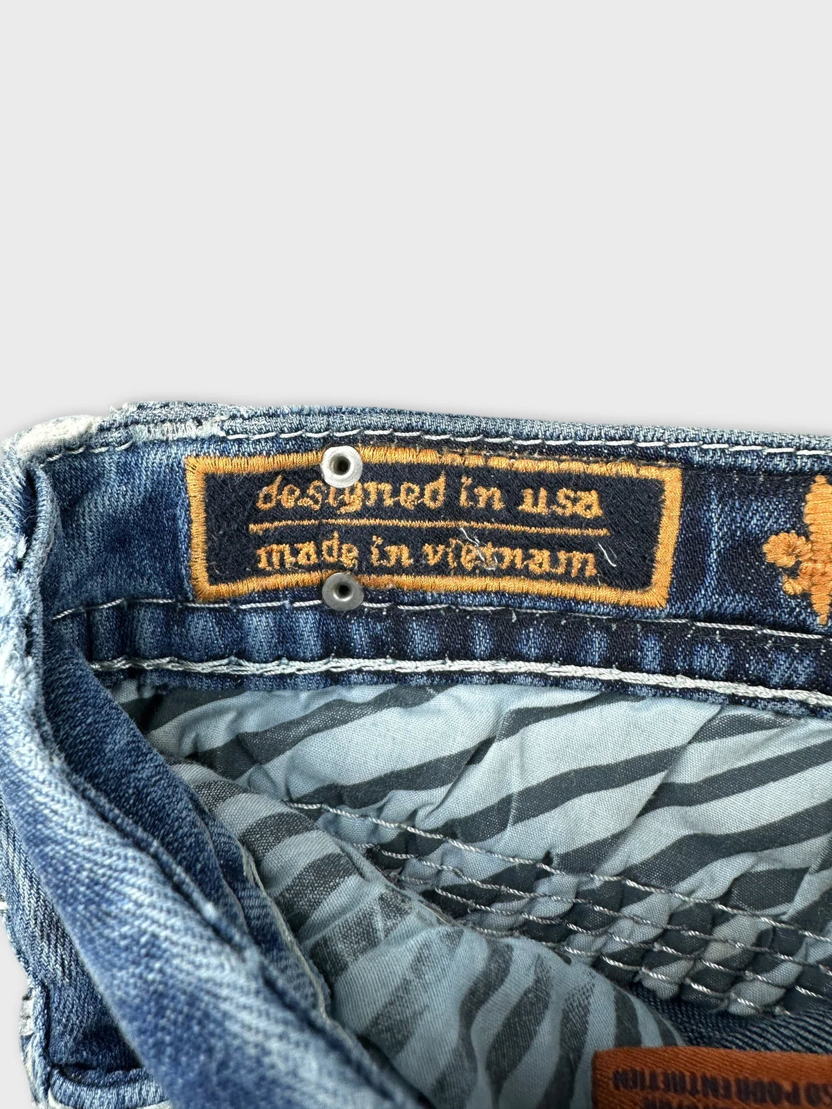 Detail view of a denim shirt featuring a colorful interior tag and striped lining.