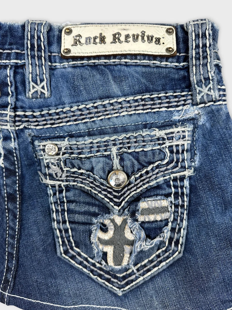 Detail view of a blue denim shirt with decorative stitching and a logo patch.