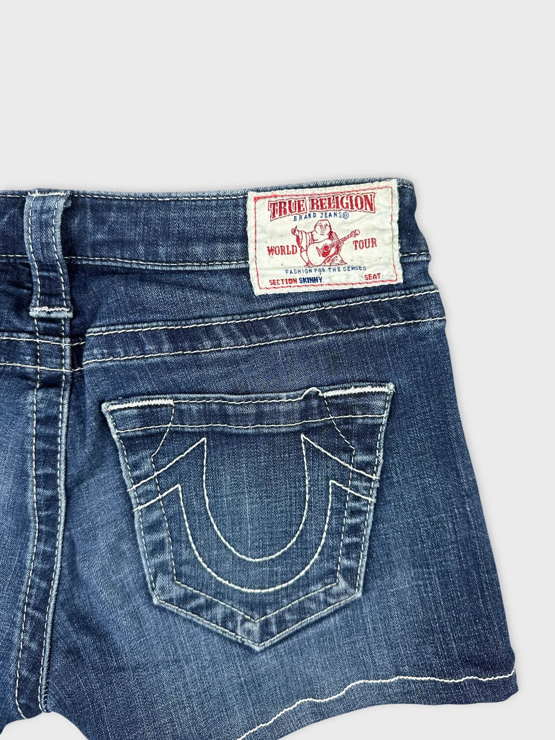 Back view of women denim shorts in dark blue with signature logo pocket detail.