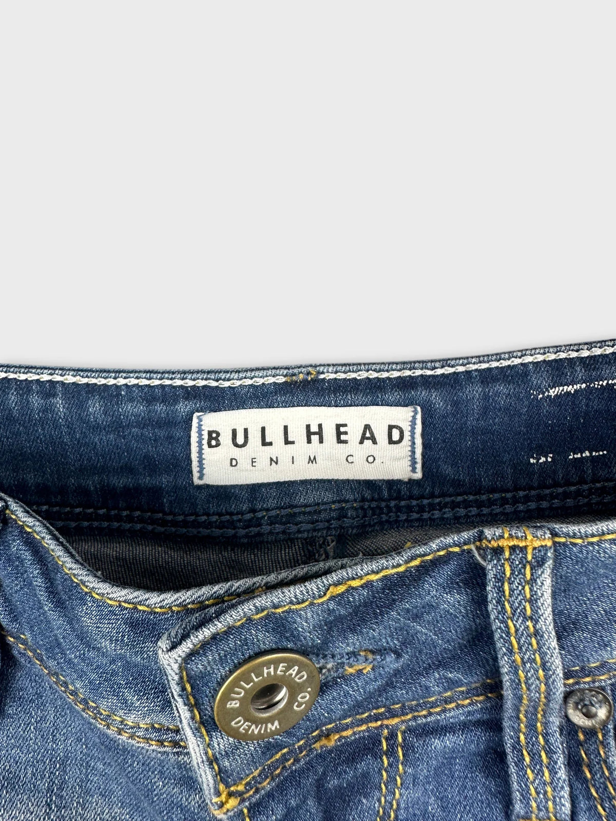 Detail view of blue denim shorts with yellow stitching and button closure.