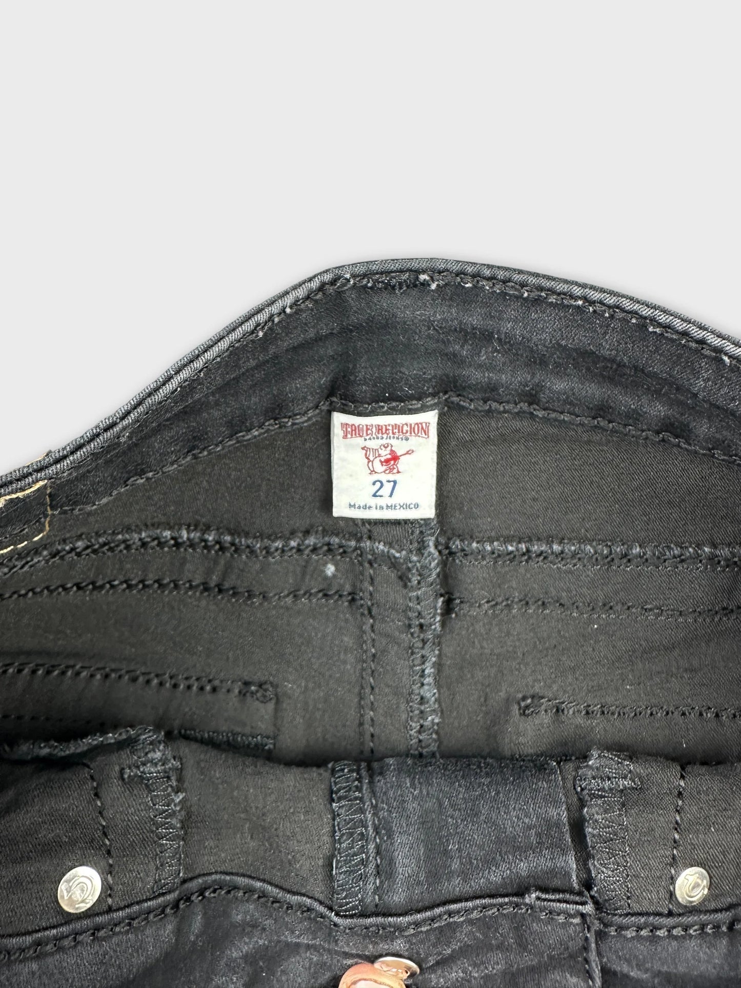 Detail view of black denim shorts showcasing waistband stitching and tag.