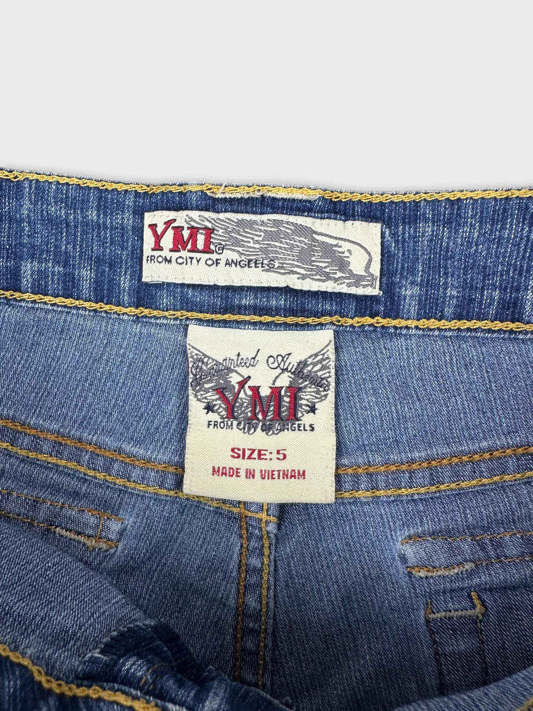 Detail view of women denim shorts featuring yellow stitching and branded tags.