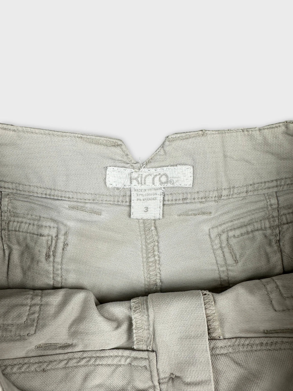 Detail view of beige denim shorts featuring a belt loop and tag.