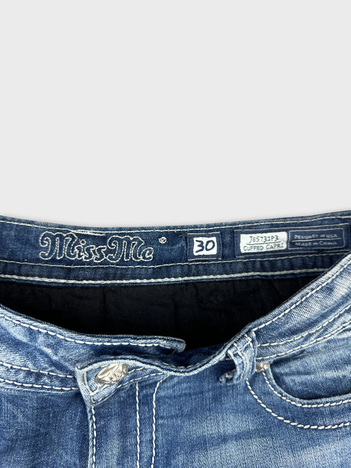 Detail view of women's denim shorts in blue with silver button and stitching.