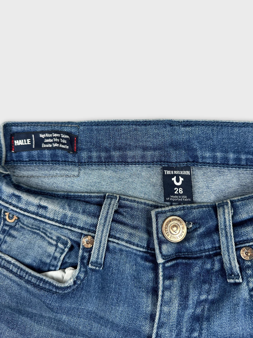 Detail view of high rise denim shorts in blue with button closure and pockets.