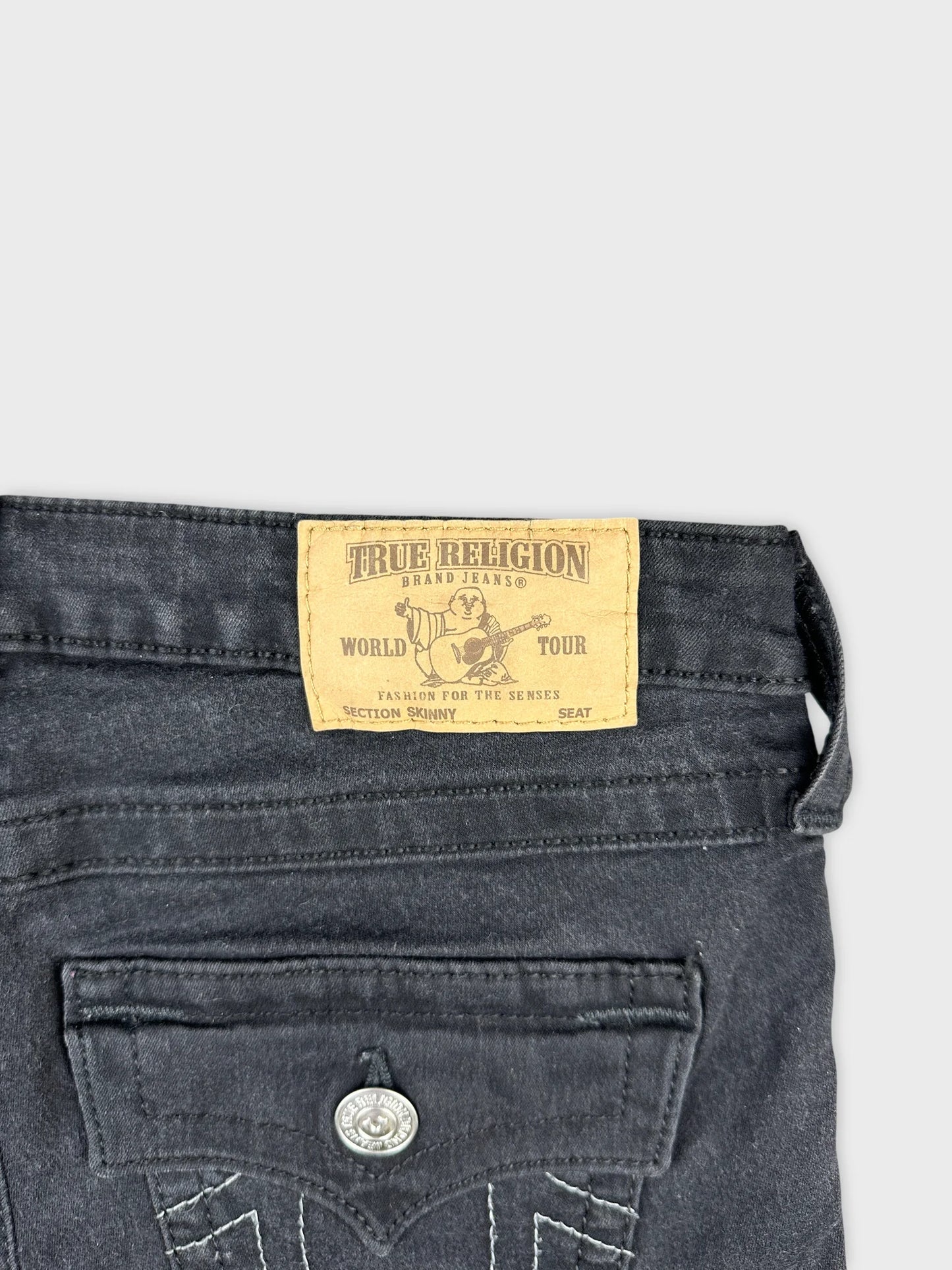 Detail view of black denim shorts featuring True Religion brand label.