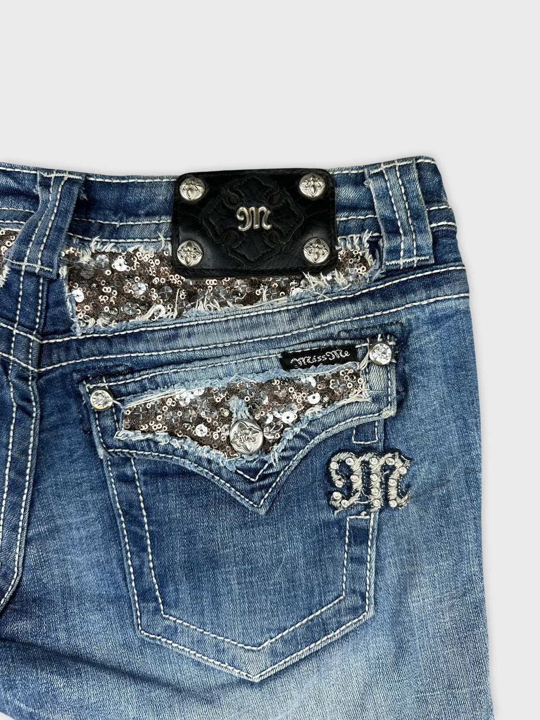 Detail view of blue denim shorts featuring sequined pocket design.