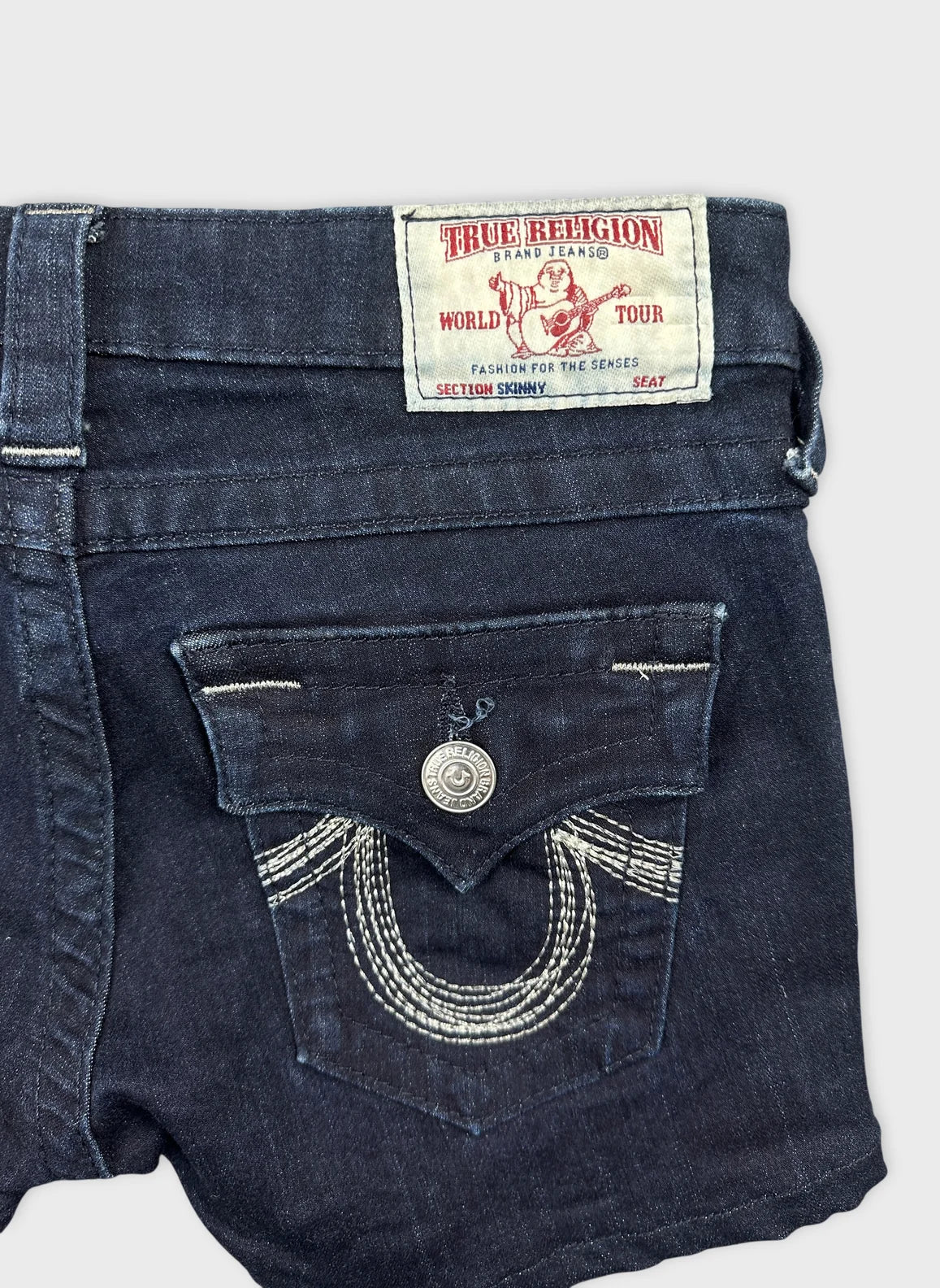 Detail view of women's denim shorts in dark blue with embroidered pocket design.