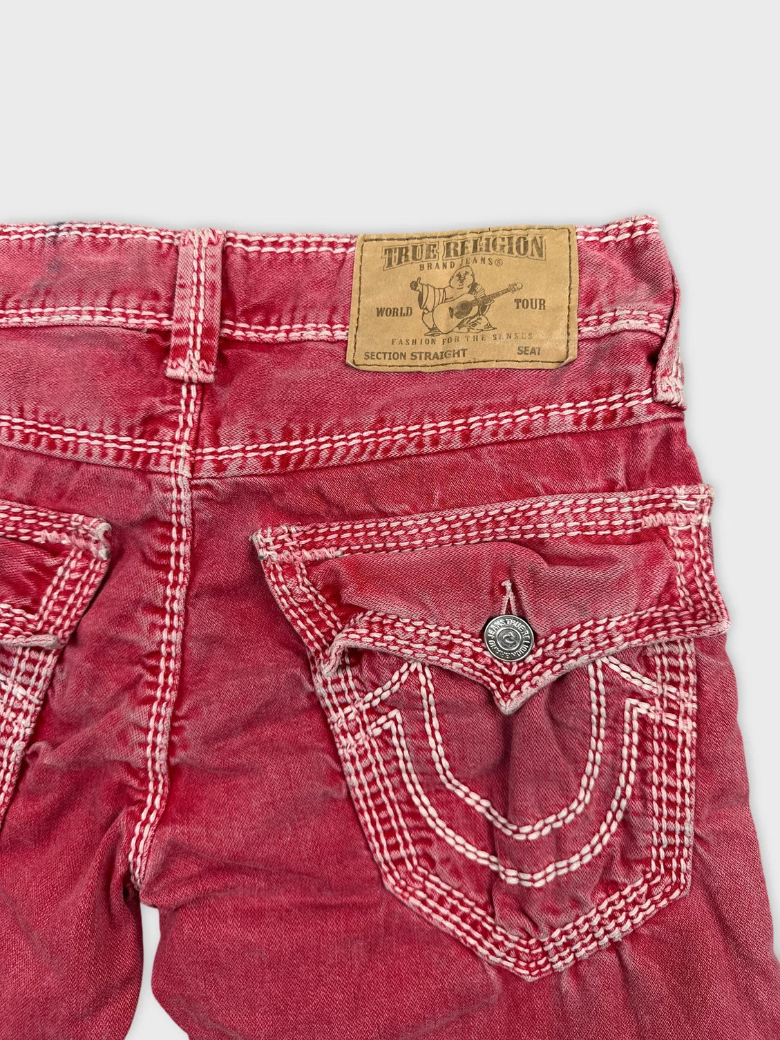 Detail view of red denim shorts featuring distinctive stitch patterns and pockets.