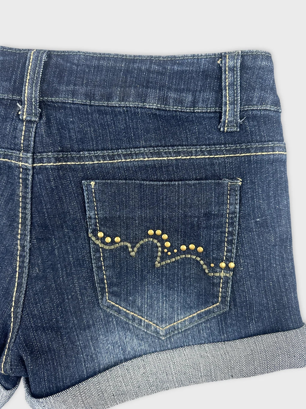 Detail view of denim shorts with gold studded pocket design and cuffed hem.