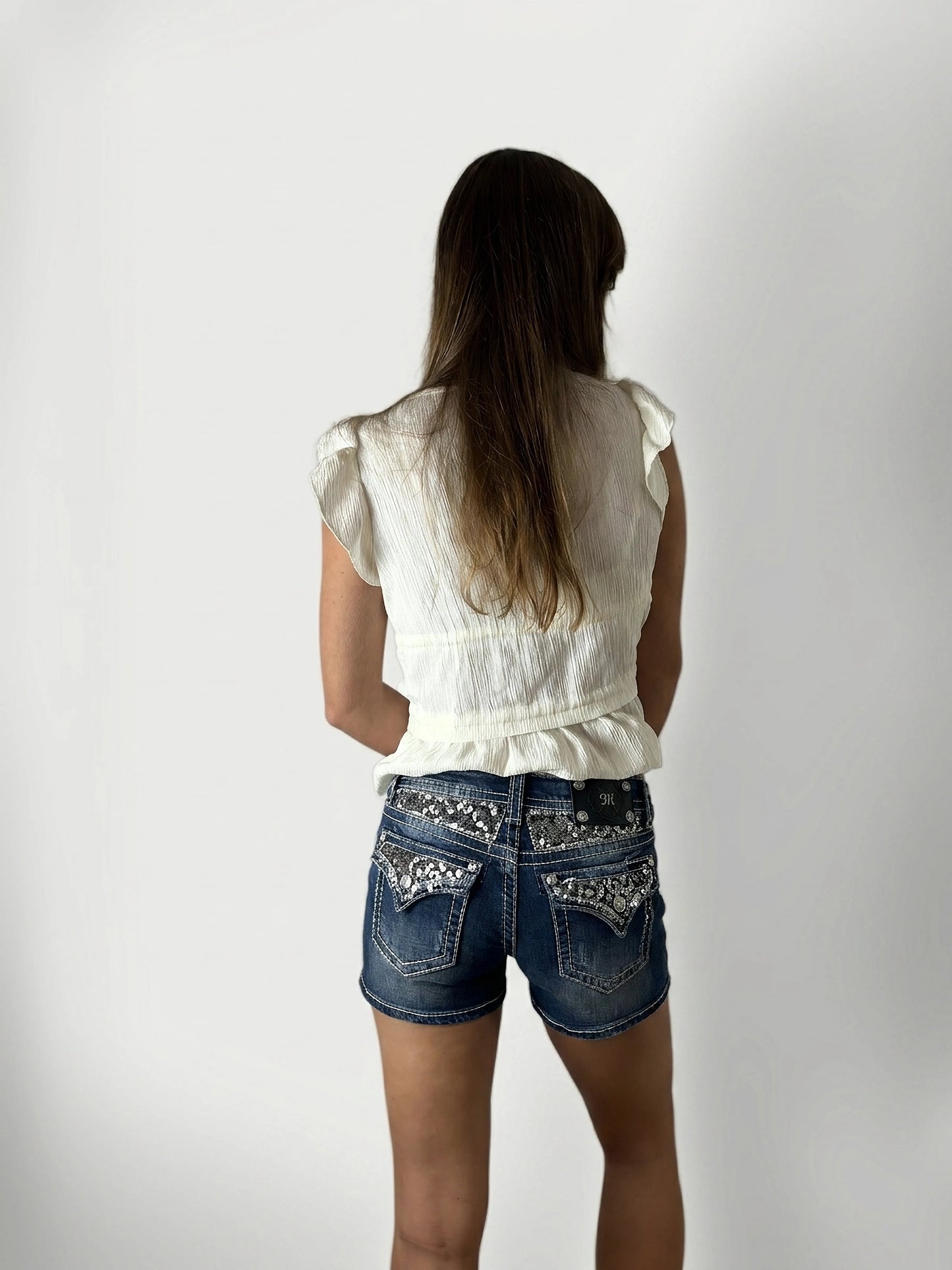 Back view of women's denim shorts in dark blue with embellished pockets.