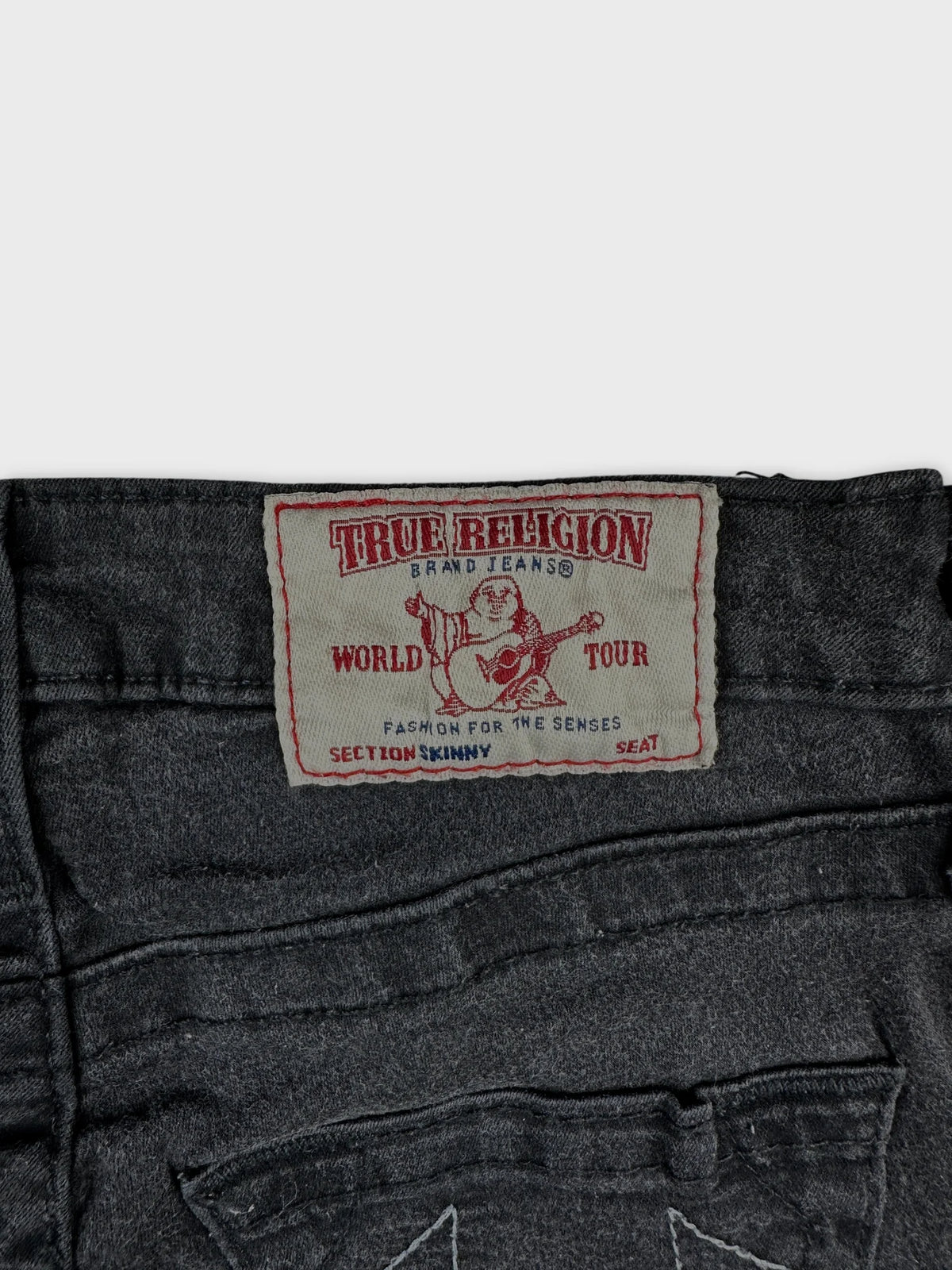 Detail view of black denim skirt featuring True Religion label.
