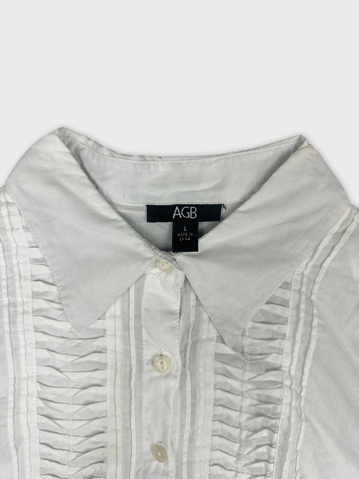 Detail view of a white long sleeve button up shirt featuring front pleating.