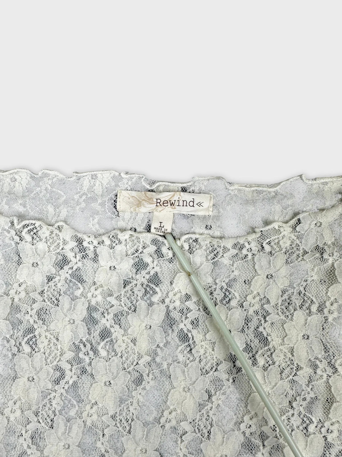 Detail view of a white lace long sleeve top with floral pattern.