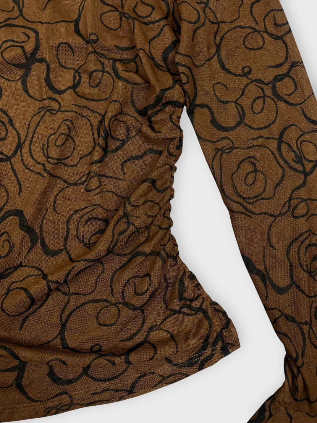 Detail view of a brown long sleeve top with black swirled pattern.