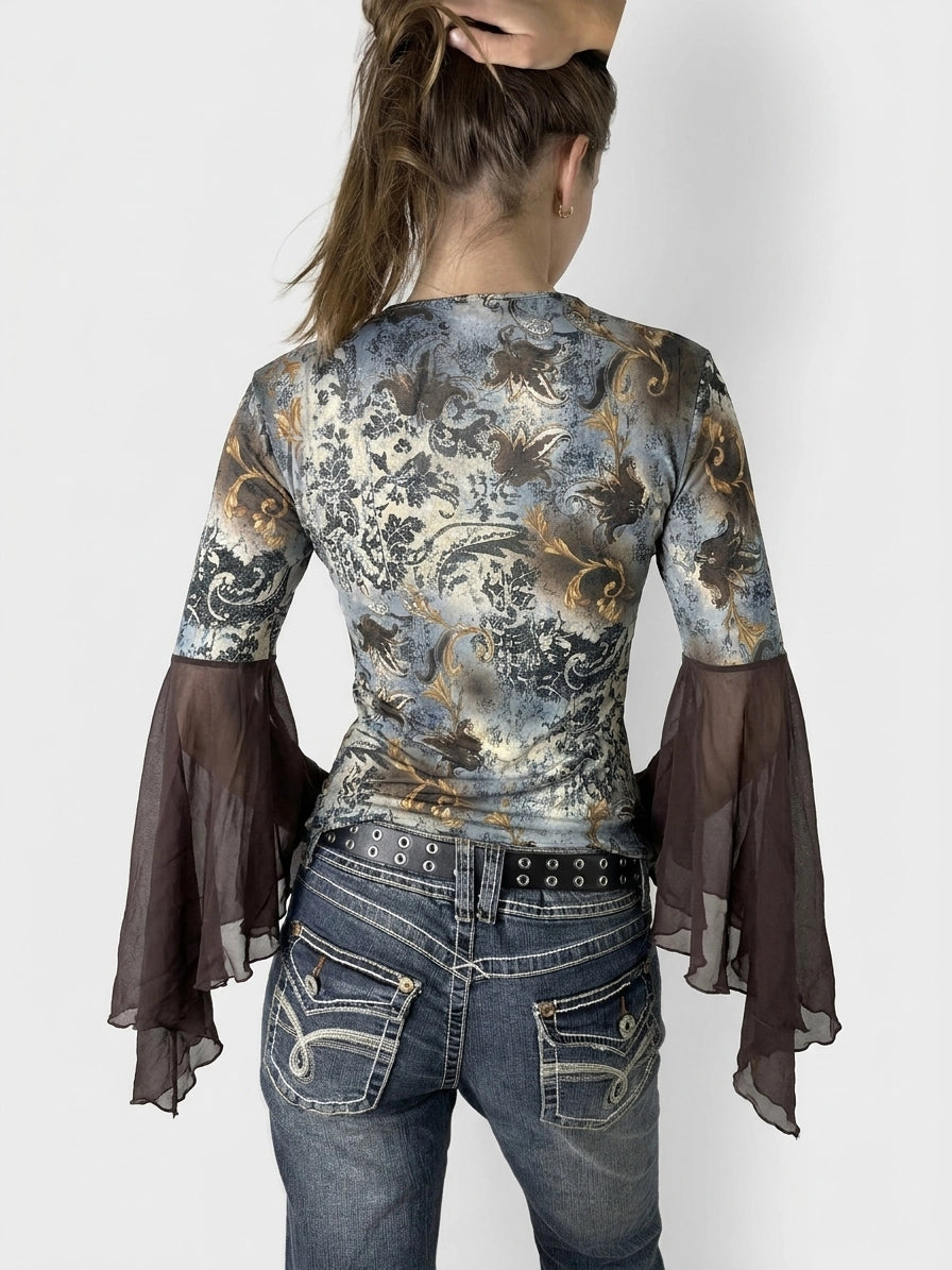 Back view of a long sleeve top in blue with sheer black bell sleeves.
