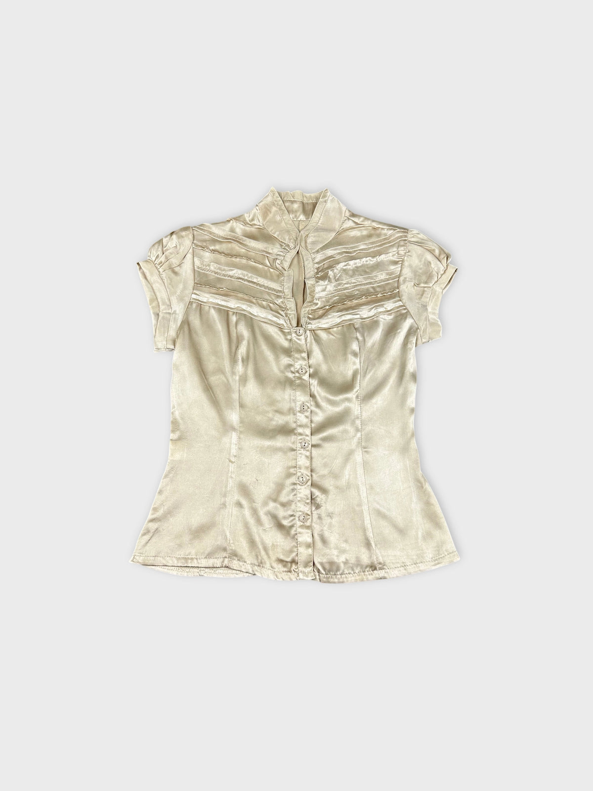 Front view of a short sleeve button up shirt in cream color with pleated detail.
