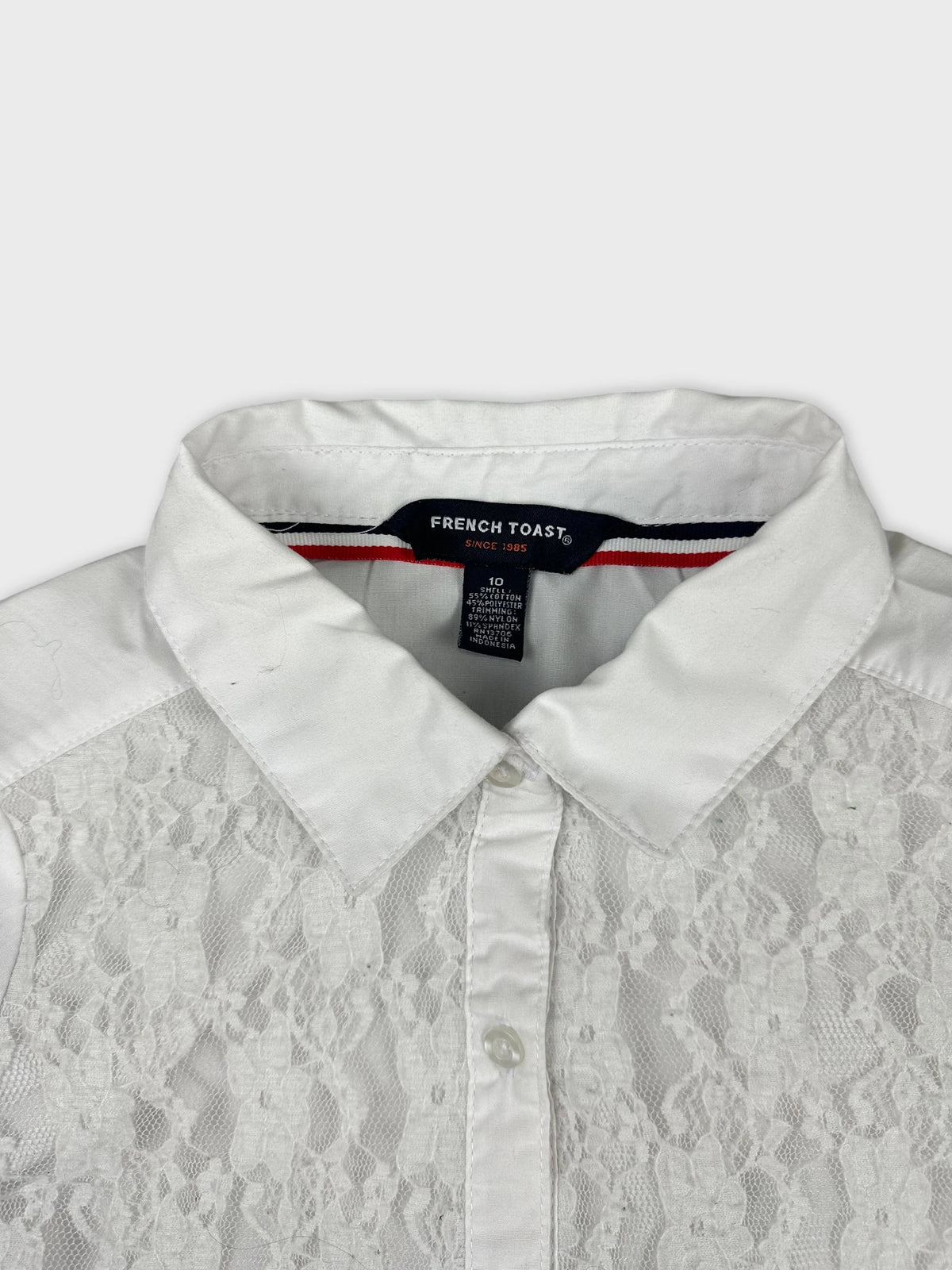 Detail view of a white women's shirt featuring lace panels and a classic collar.