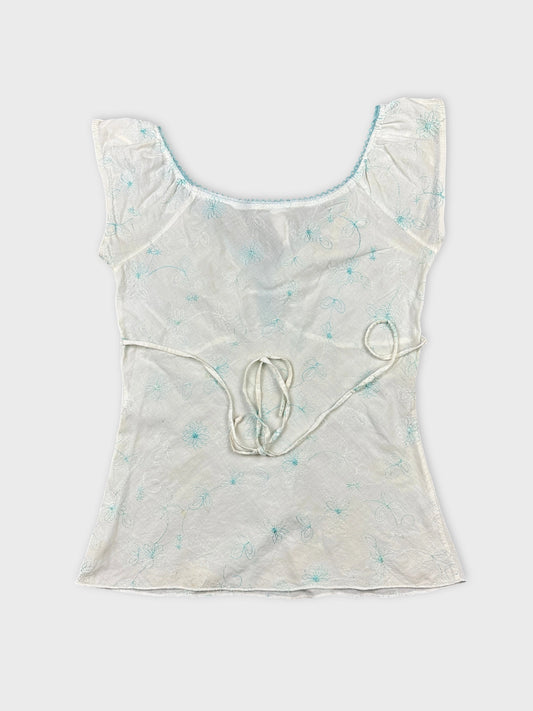 Back view of a white short sleeve top with blue floral embroidery.