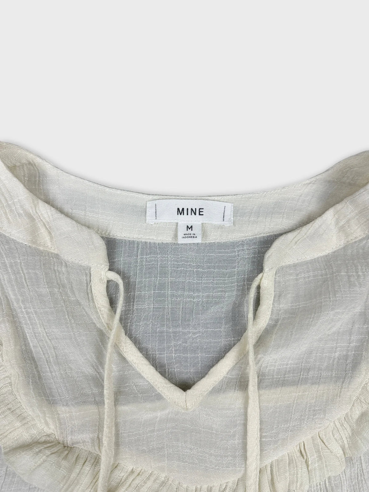 Detail view of a cream short sleeve top with a ruffled neckline