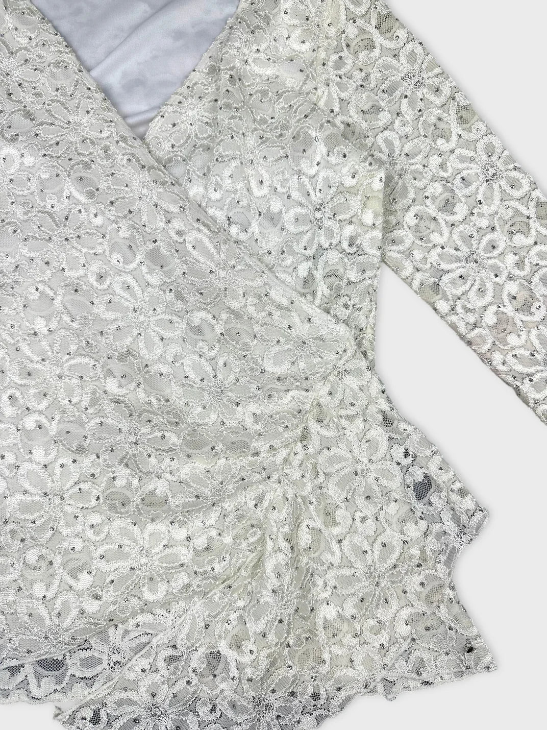 Detail view of white vintage lace top with floral pattern and wrap design.