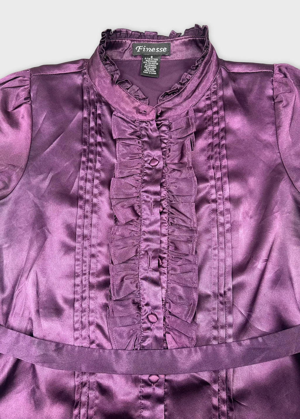 Detail view of a purple button-up shirt featuring ruffled front and collar.