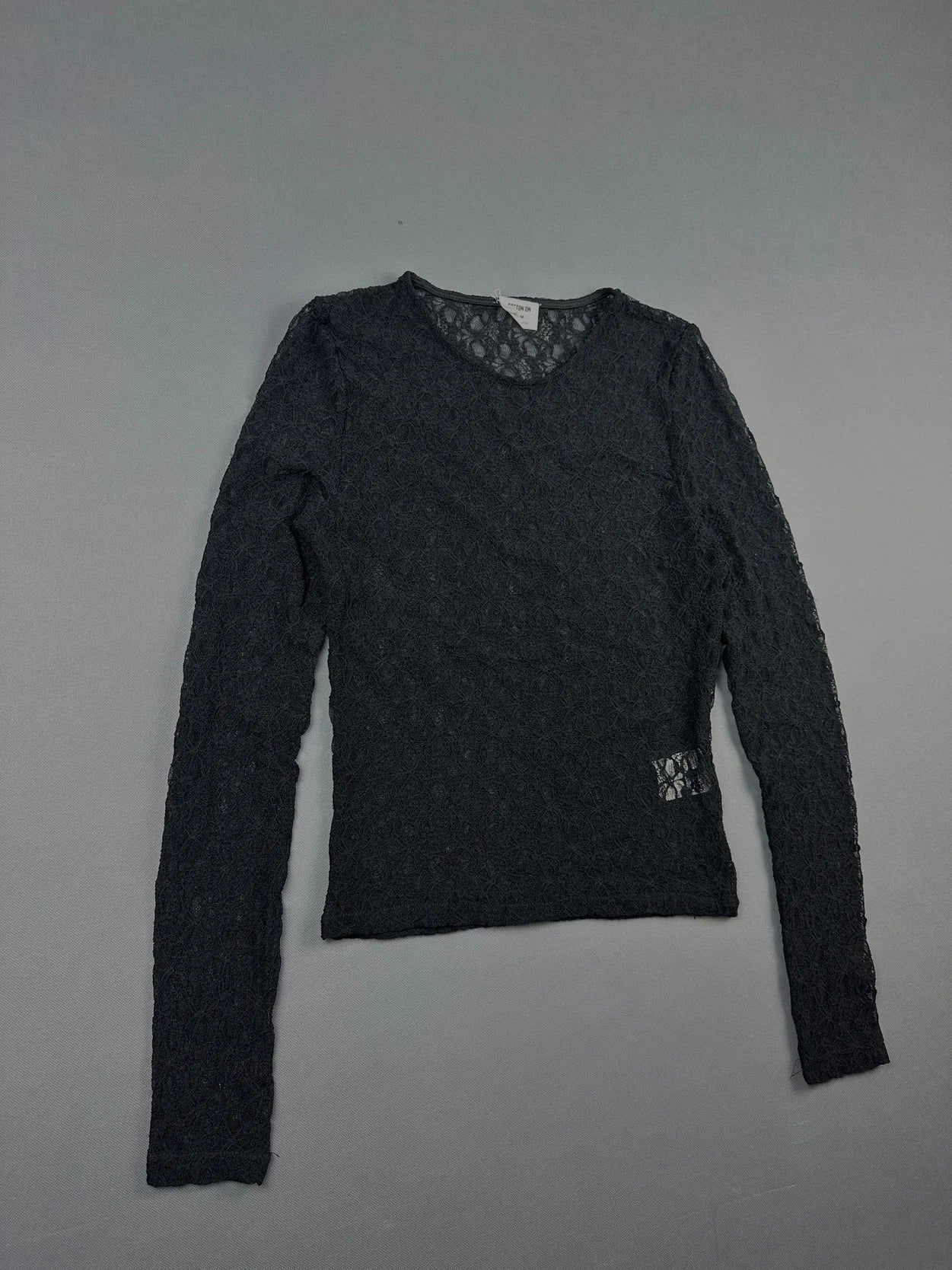 Black long sleeve top detail view featuring floral lace pattern.