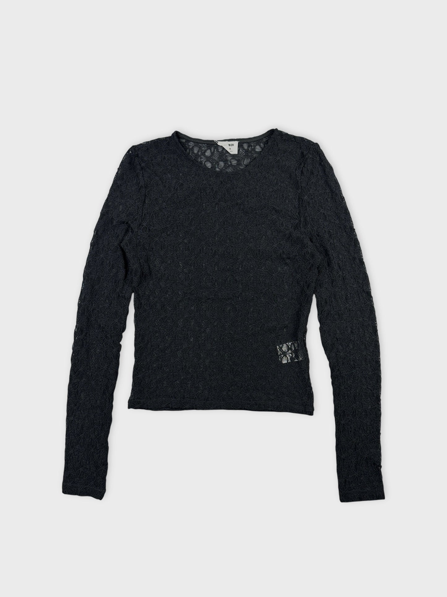 Front view of a black long sleeve top featuring intricate lace pattern.
