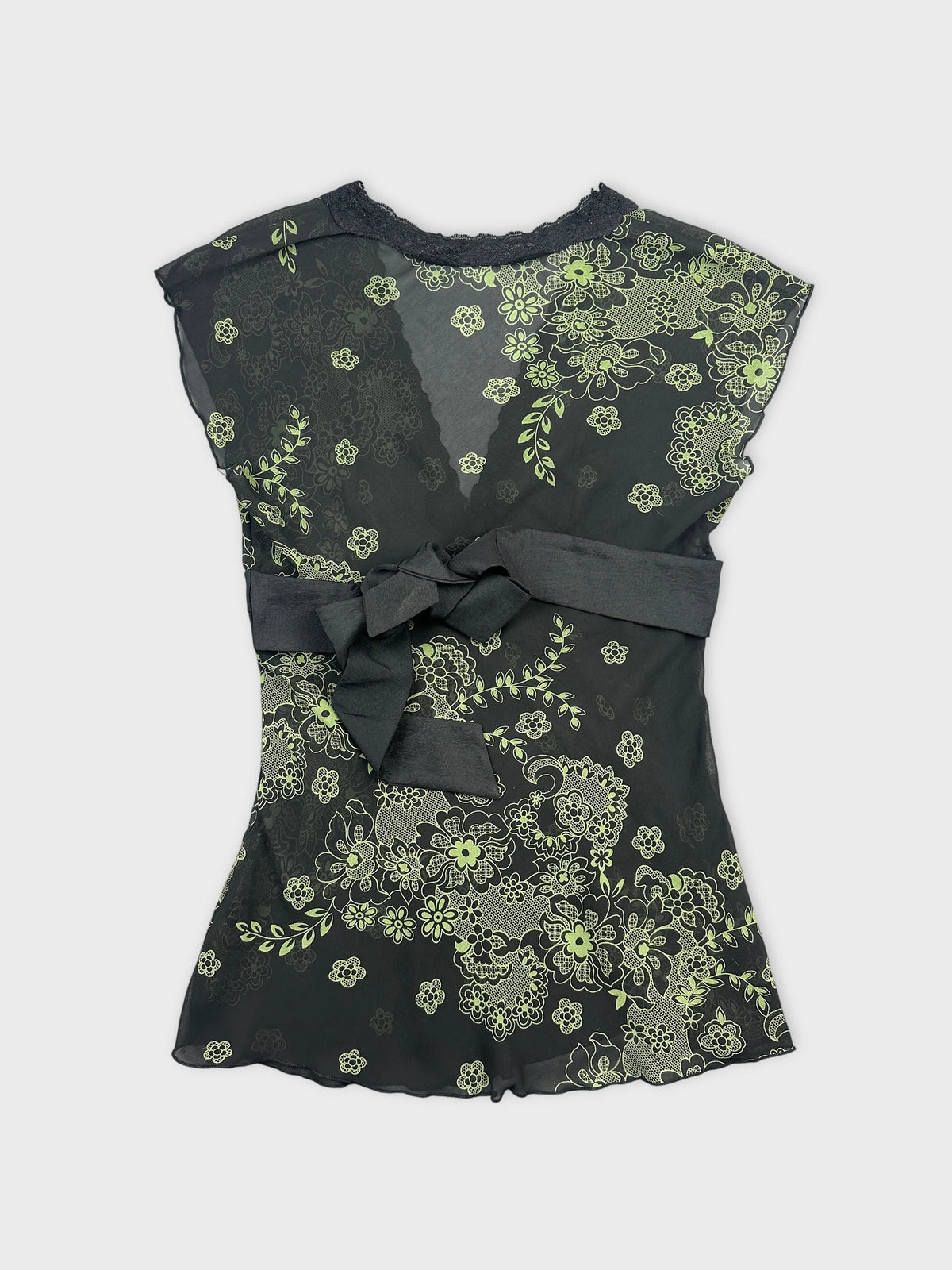 Back view of a black vintage top with green floral prints and bow detail.