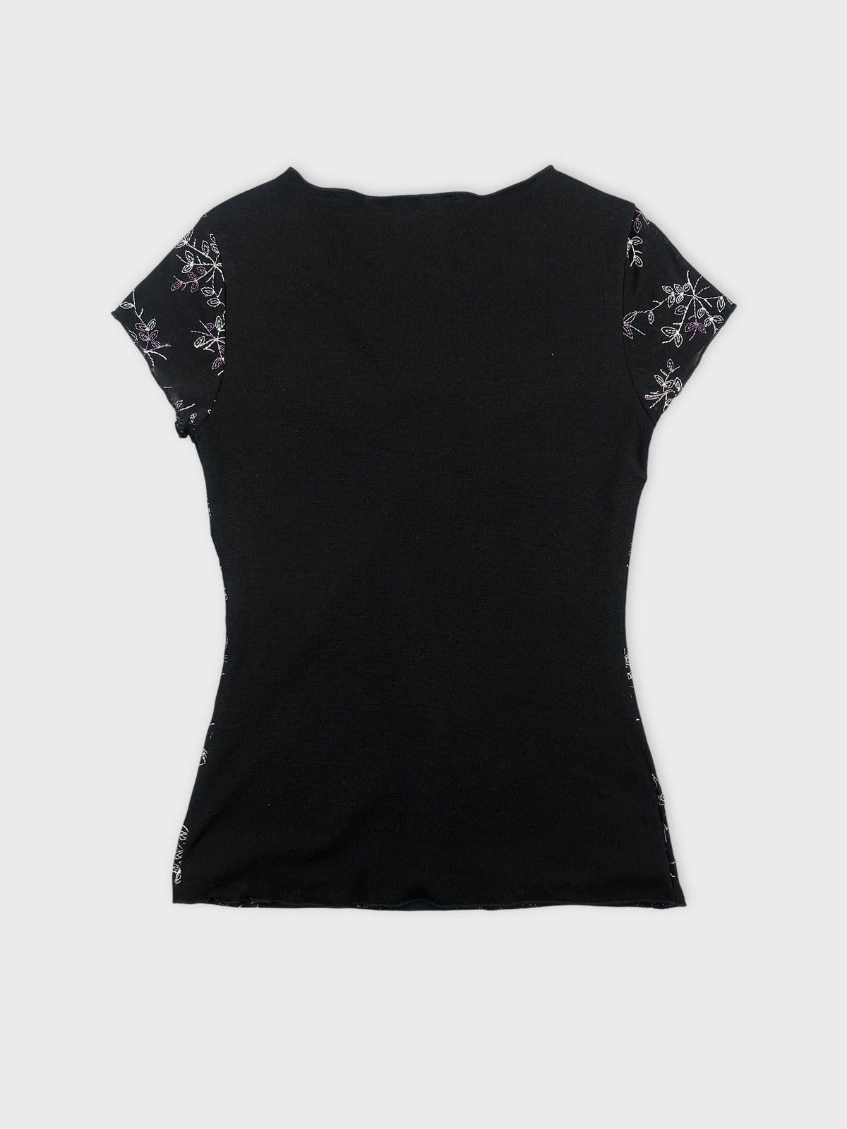 Back view of a black women’s top with floral embroidered sleeves.