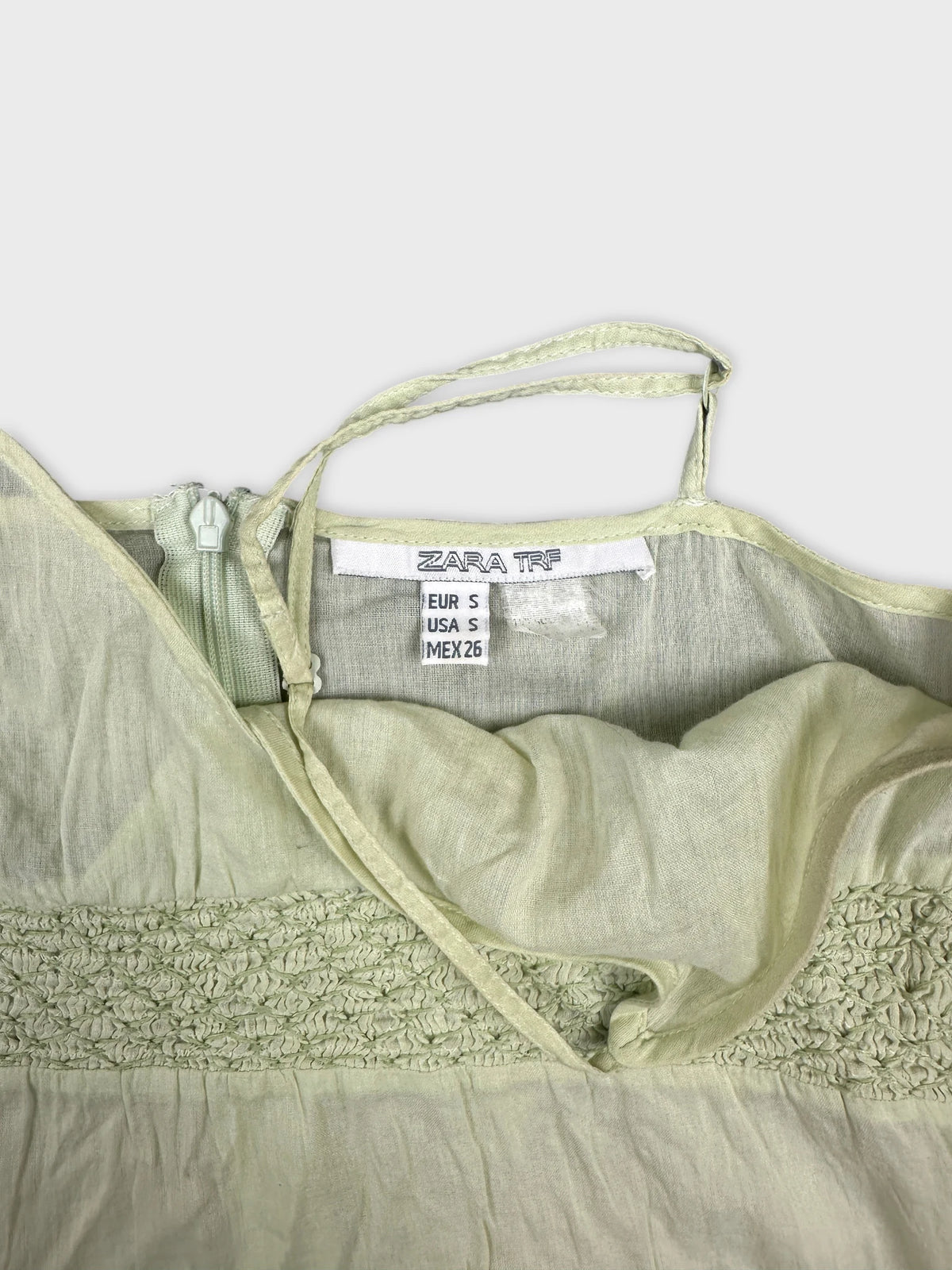 Detail view of a light green top featuring smocked texture and zipper