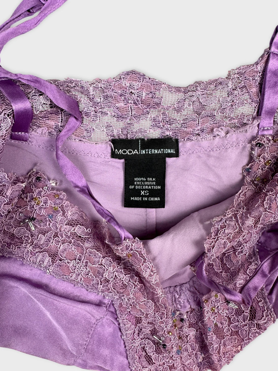 Detail view of a purple silk top featuring lace trim and decorative embellishments.