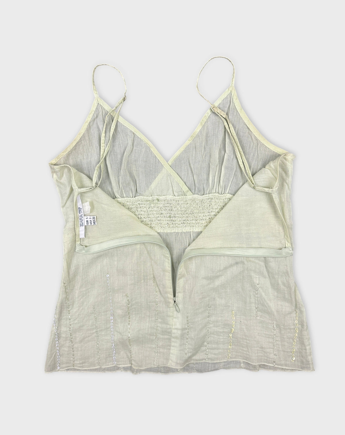 Detail view of a light green women's top with a zip and sequined accents.