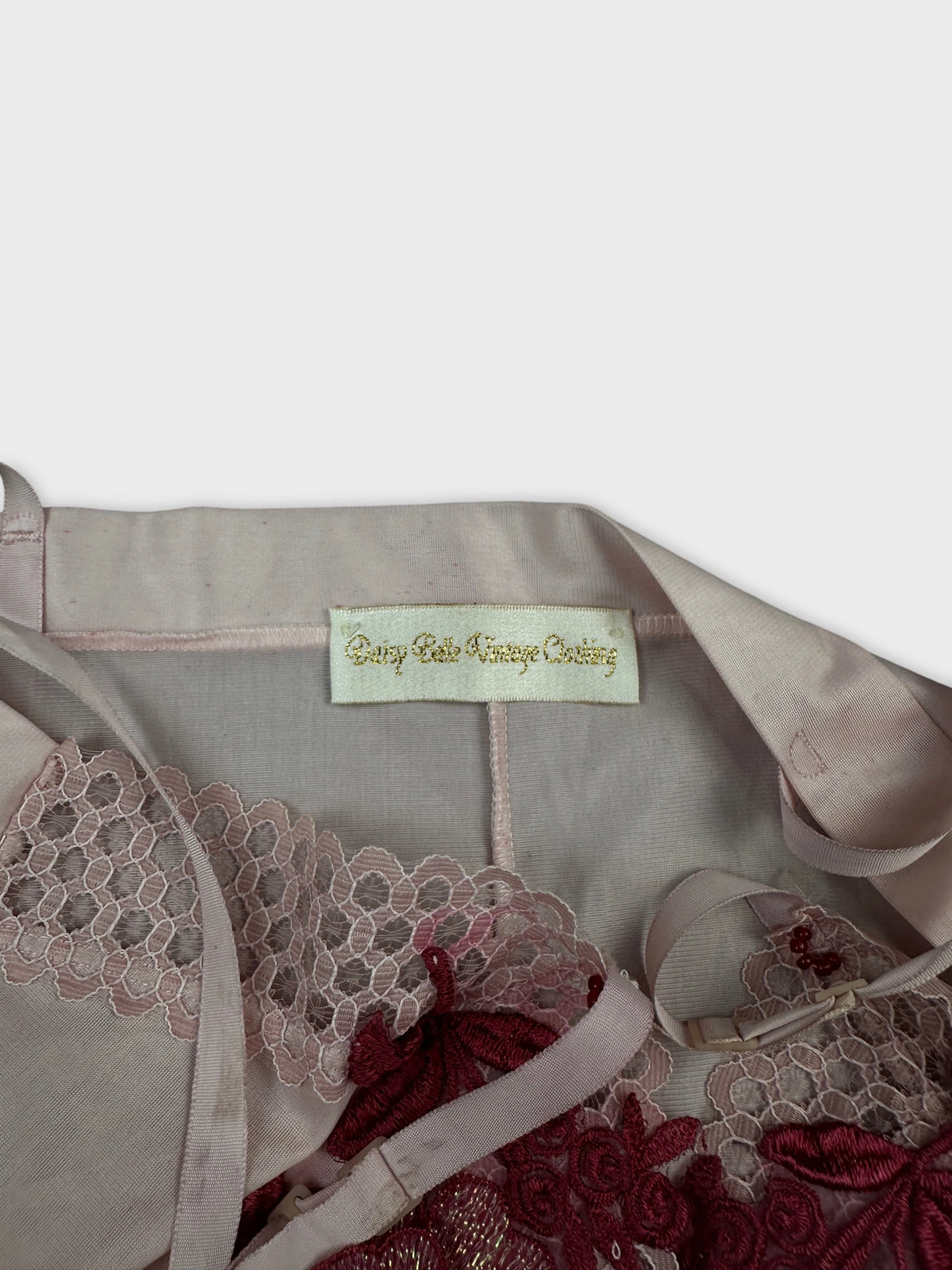 Detail view of a pink vintage top featuring lace trim and intricate embroidery.