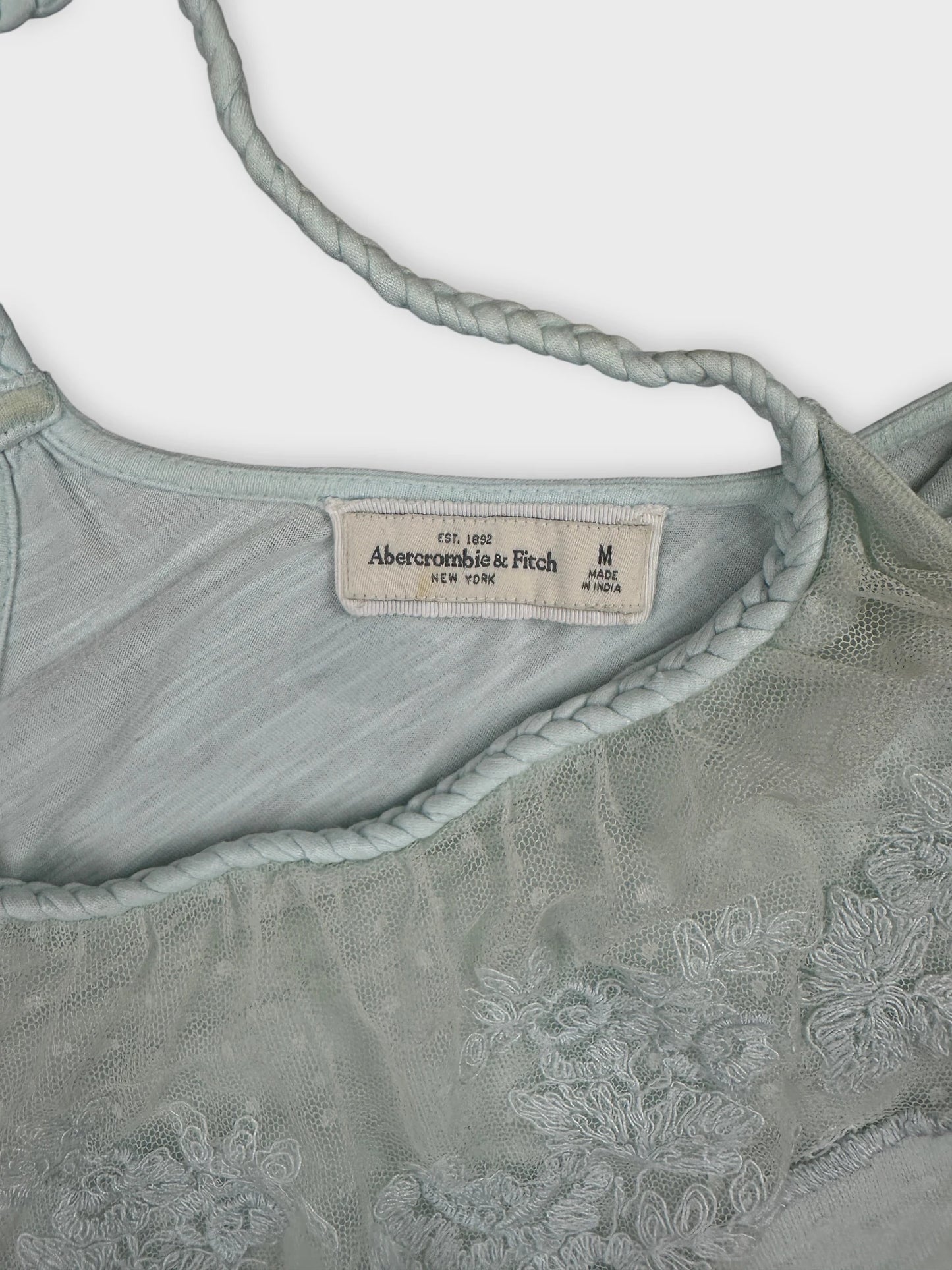 Detail view of a light green vintage top featuring lace trim and embroidered patterns.