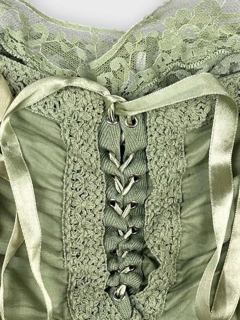 Detail view of a green vintage top featuring lace trim and ribbon lacing.