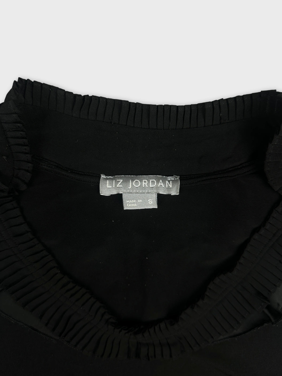 Black top with ruffled neckline, detail view.
