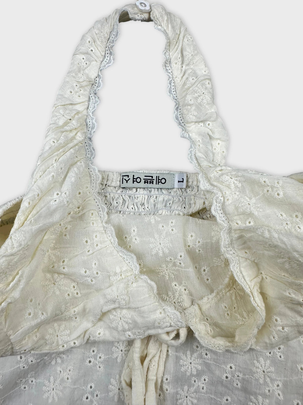 Detail view of a vintage white upper body top with floral embroidery and lace trim.