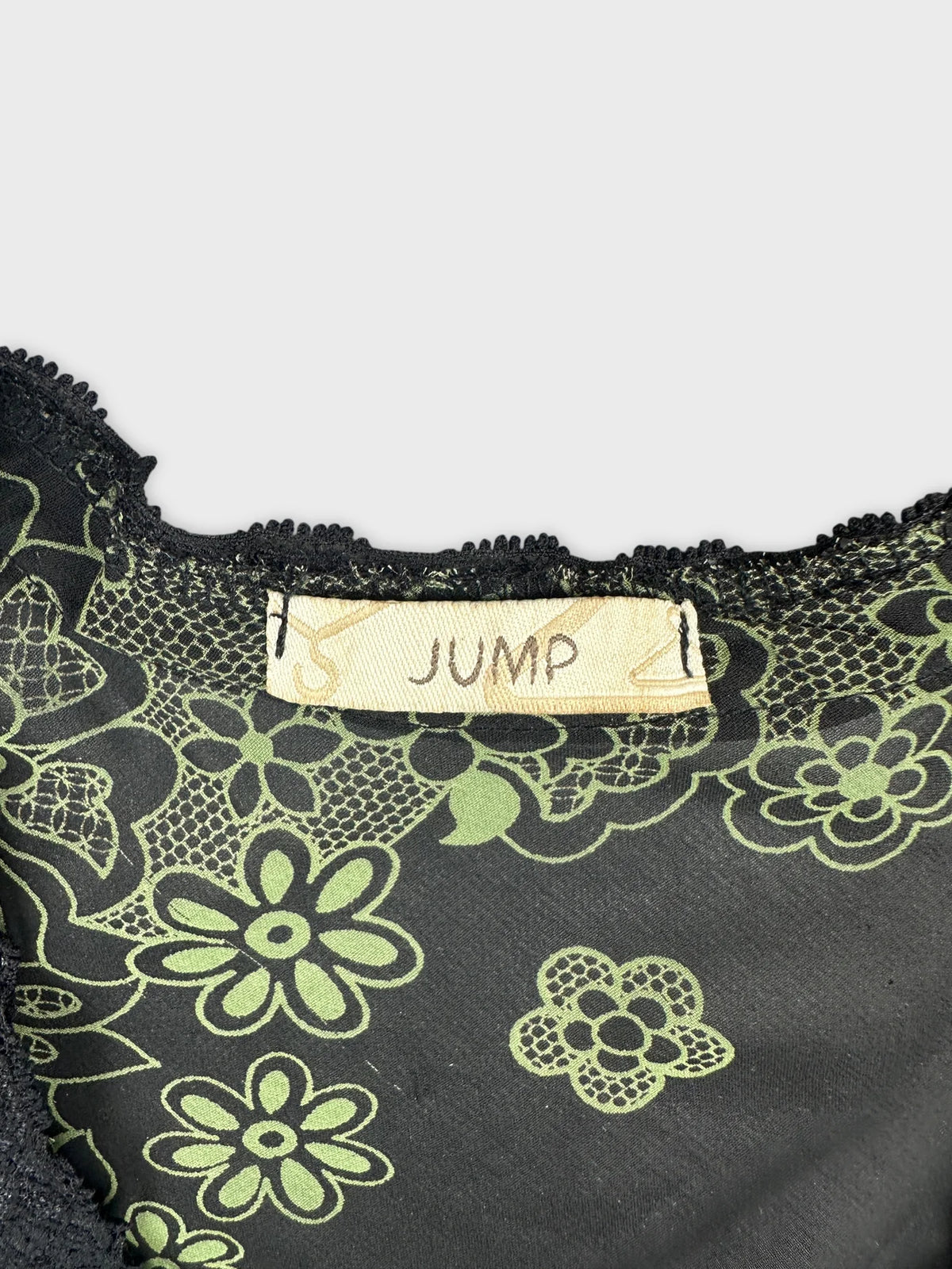 Detail view of a black vintage top with green floral print and lace trim