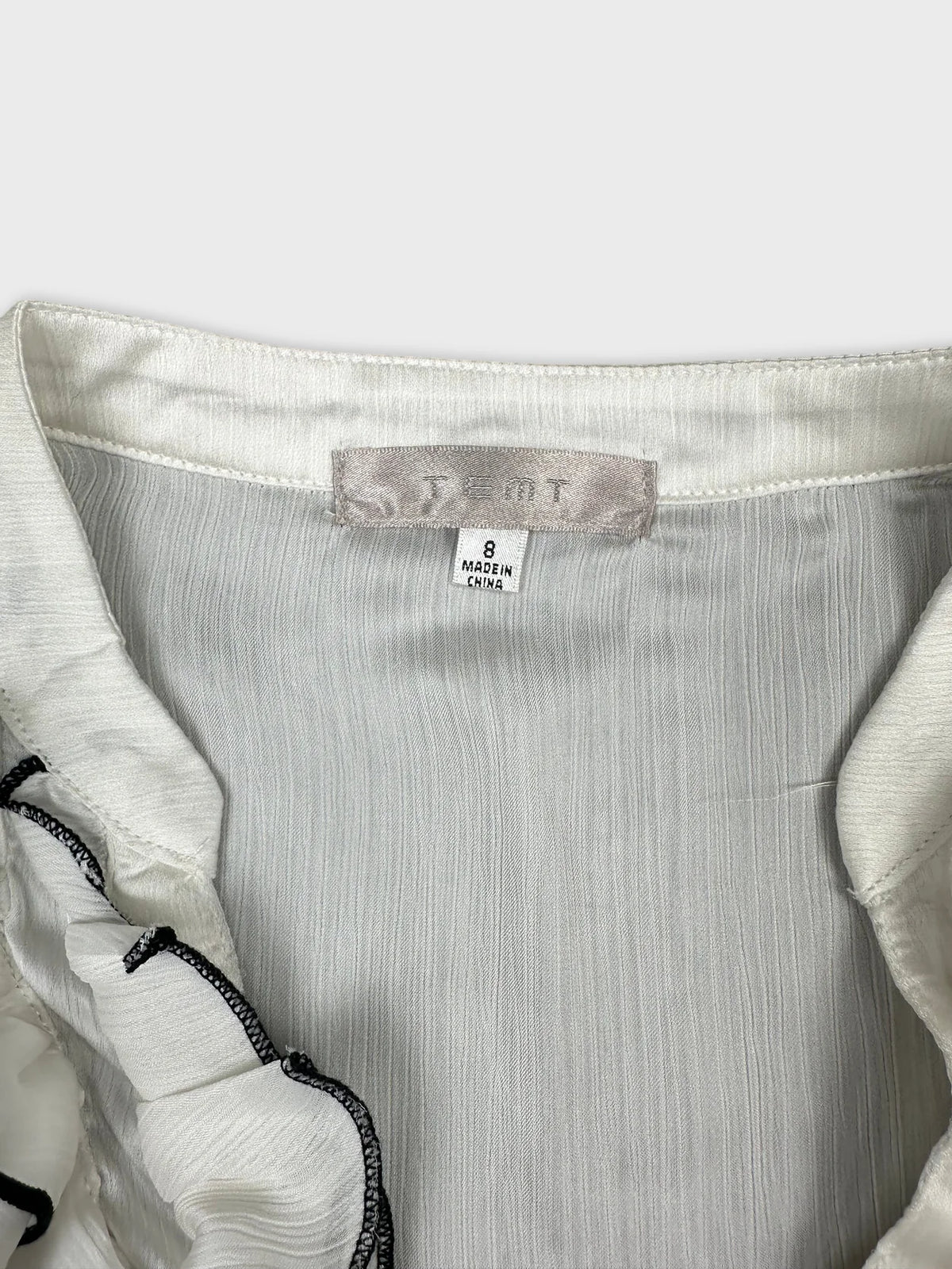 Detail view of a white vintage upper body top with ruffled trim.